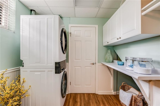 clothes washing area with cabinets, stacked washer / drying machine, and wood-type flooring