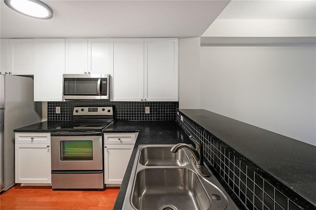 kitchen featuring appliances with stainless steel finishes, tasteful backsplash, white cabinets, light hardwood / wood-style flooring, and sink