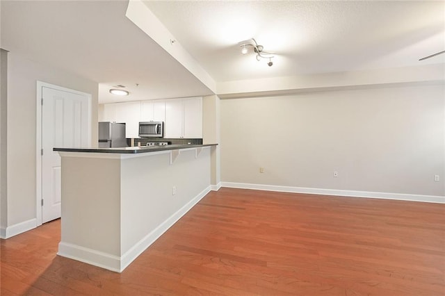 kitchen featuring light wood-type flooring, white cabinets, kitchen peninsula, a kitchen bar, and stainless steel appliances