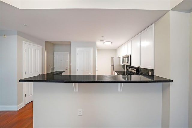 kitchen featuring white cabinetry, kitchen peninsula, a kitchen breakfast bar, appliances with stainless steel finishes, and hardwood / wood-style floors