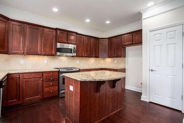 kitchen with a kitchen island, light stone countertops, appliances with stainless steel finishes, and dark wood-type flooring