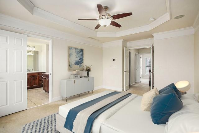 carpeted bedroom featuring ceiling fan, ensuite bath, ornamental molding, and a raised ceiling