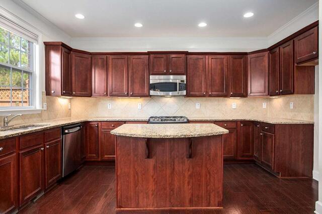 kitchen with light stone counters, appliances with stainless steel finishes, a center island, and sink