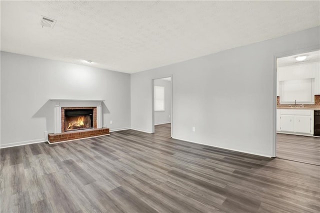 unfurnished living room with wood finished floors, a sink, a fireplace, a textured ceiling, and baseboards