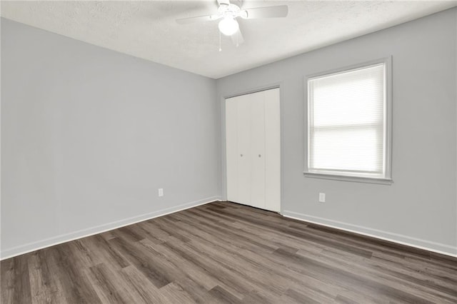 unfurnished bedroom featuring wood finished floors, a textured ceiling, a closet, baseboards, and a ceiling fan