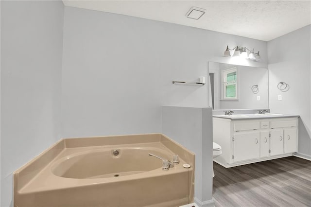 bathroom with a garden tub, wood finished floors, double vanity, toilet, and a textured ceiling