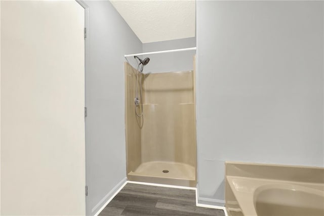 bathroom with wood finished floors, a shower stall, a textured ceiling, baseboards, and a bath