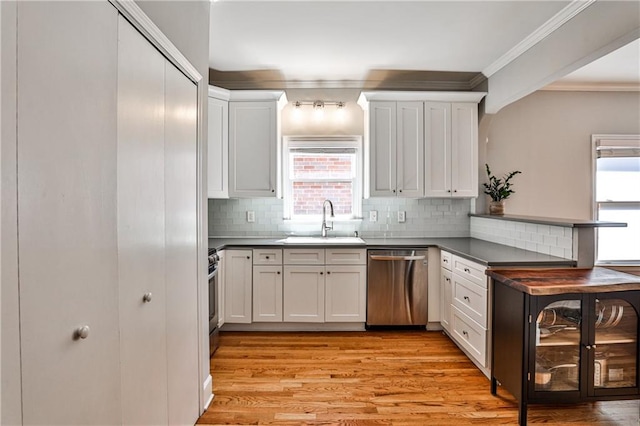 kitchen with light wood-type flooring, a sink, dark countertops, stainless steel appliances, and crown molding