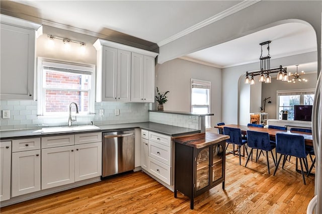 kitchen with light wood-type flooring, a sink, stainless steel dishwasher, dark countertops, and a peninsula