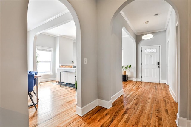 foyer entrance featuring arched walkways, wood finished floors, baseboards, and ornamental molding