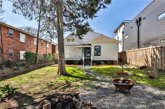 rear view of property with a lawn, a porch, an outdoor fire pit, and fence