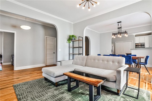 living room featuring baseboards, light wood-type flooring, ornamental molding, arched walkways, and a notable chandelier