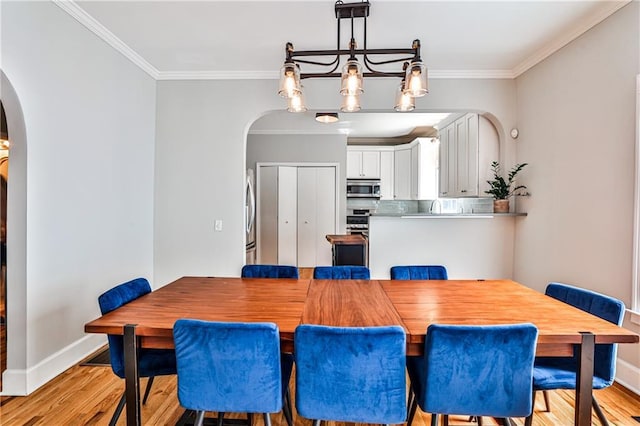 dining space featuring light wood-type flooring, arched walkways, baseboards, and ornamental molding