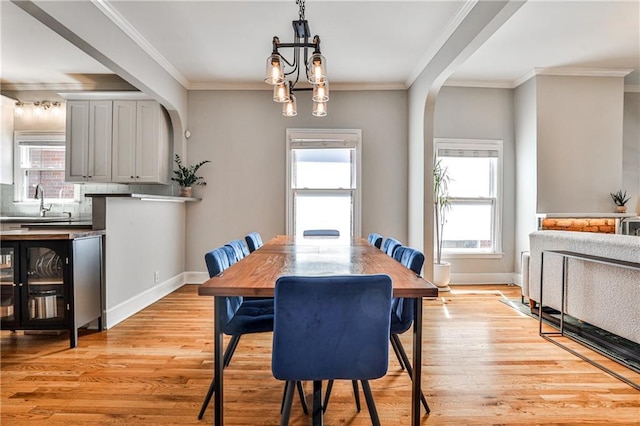 dining area with light wood-style flooring, baseboards, arched walkways, and ornamental molding