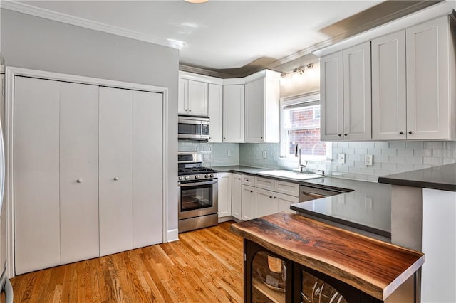 kitchen with a sink, dark countertops, stainless steel appliances, light wood-style floors, and decorative backsplash