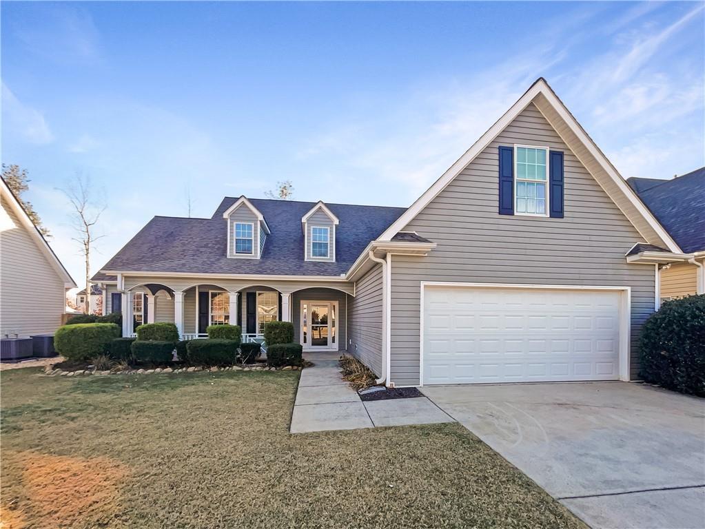 view of front of home featuring a garage, covered porch, a front yard, and cooling unit