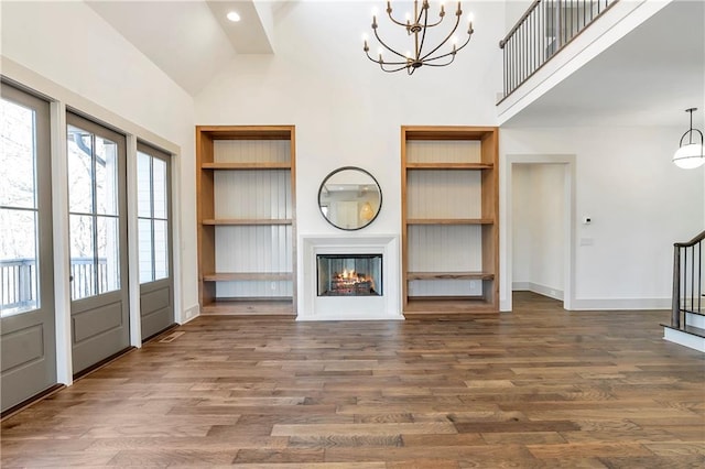 unfurnished living room with a notable chandelier, high vaulted ceiling, built in features, and dark hardwood / wood-style flooring