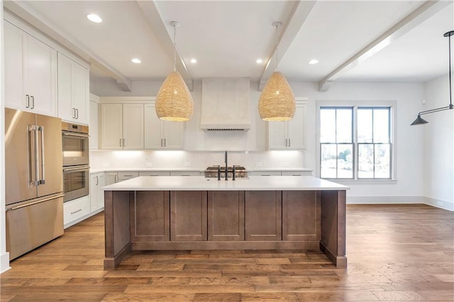 kitchen featuring appliances with stainless steel finishes, hardwood / wood-style floors, an island with sink, custom range hood, and beam ceiling