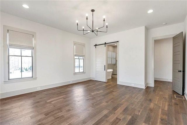 unfurnished bedroom with multiple windows, a barn door, dark hardwood / wood-style floors, and a notable chandelier