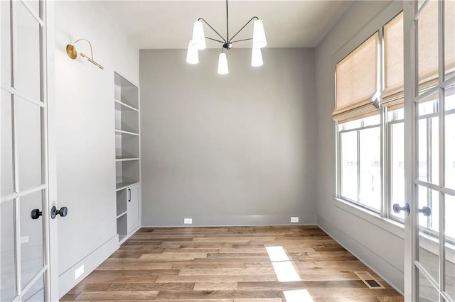 unfurnished room with an inviting chandelier, light hardwood / wood-style flooring, and french doors