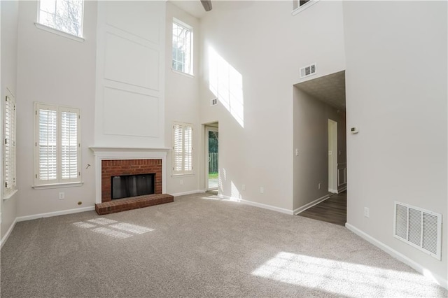 unfurnished living room with a fireplace, carpet flooring, visible vents, and a healthy amount of sunlight