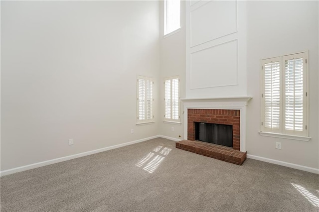 unfurnished living room with a towering ceiling, baseboards, a wealth of natural light, and carpet flooring