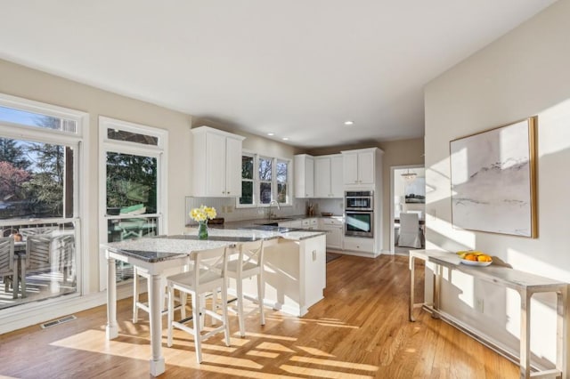 kitchen featuring tasteful backsplash, a peninsula, light wood-style floors, stainless steel double oven, and white cabinets