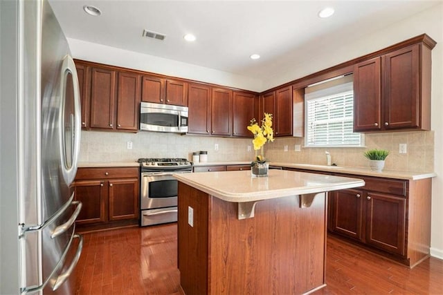 kitchen with decorative backsplash, a kitchen breakfast bar, dark hardwood / wood-style flooring, stainless steel appliances, and a center island