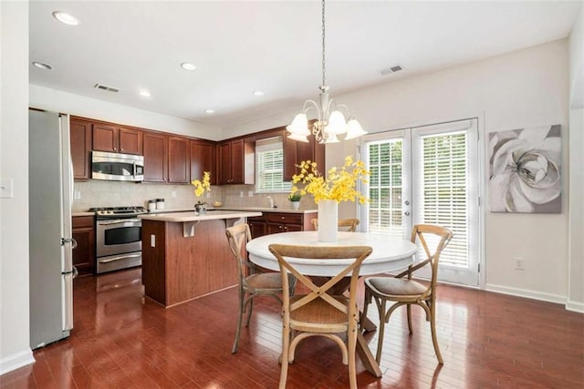 kitchen with a center island, stainless steel appliances, dark hardwood / wood-style floors, backsplash, and pendant lighting