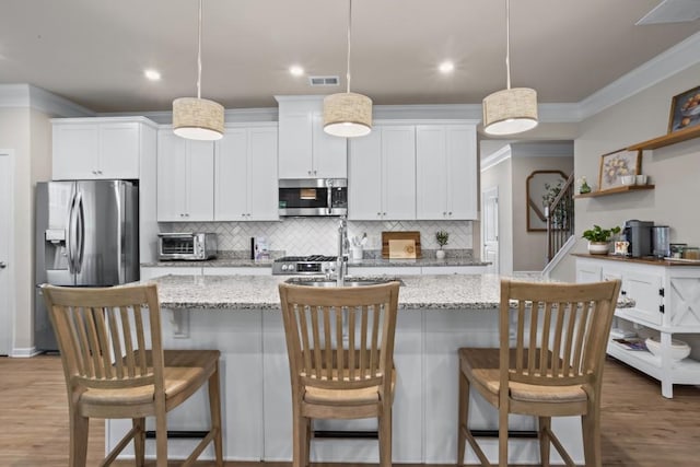 kitchen with crown molding, visible vents, appliances with stainless steel finishes, a center island with sink, and decorative backsplash