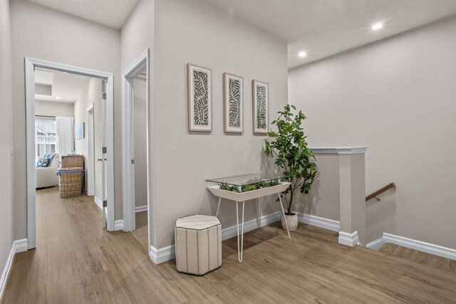 hall with wood finished floors, baseboards, an upstairs landing, and recessed lighting