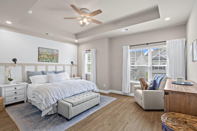bedroom featuring a tray ceiling, visible vents, recessed lighting, wood finished floors, and baseboards