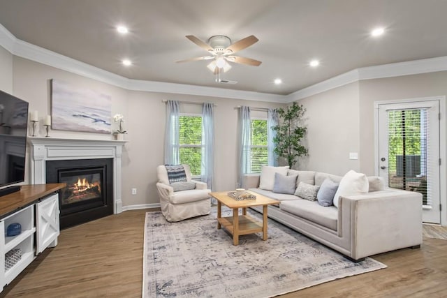 living room featuring crown molding, visible vents, wood finished floors, and a glass covered fireplace