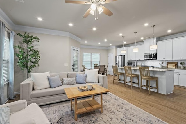 living area featuring a ceiling fan, light wood-type flooring, ornamental molding, and recessed lighting