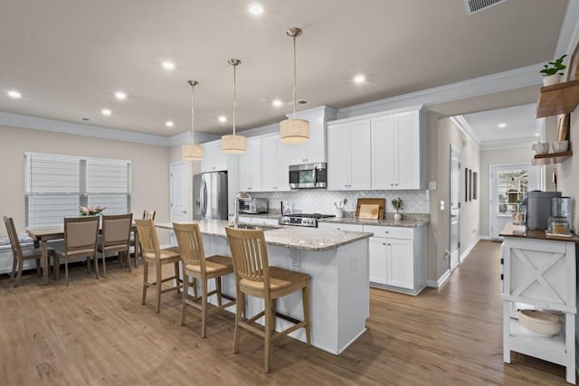kitchen featuring tasteful backsplash, ornamental molding, appliances with stainless steel finishes, wood finished floors, and a center island with sink