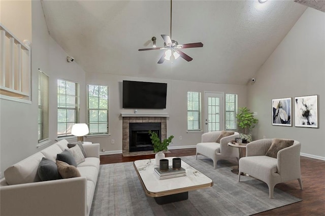 living area featuring dark wood finished floors, high vaulted ceiling, baseboards, a ceiling fan, and a tiled fireplace