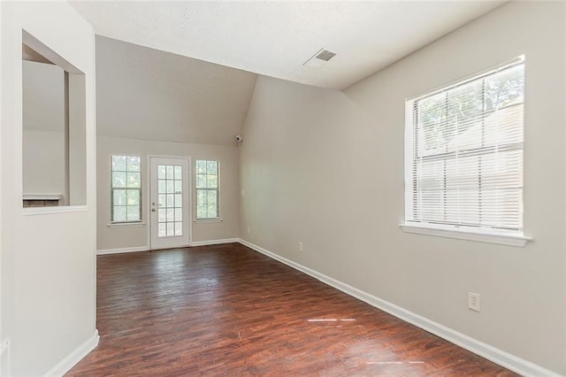 unfurnished room with healthy amount of natural light, baseboards, dark wood finished floors, and vaulted ceiling