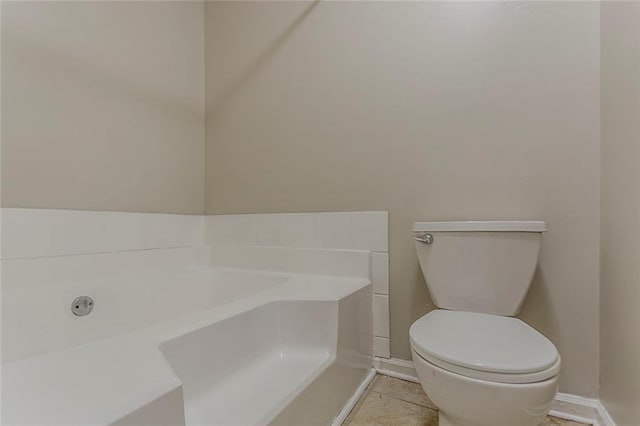 bathroom with toilet, a garden tub, and baseboards