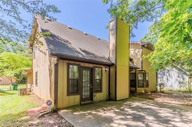 rear view of property featuring a shingled roof, a chimney, a patio, and central air condition unit