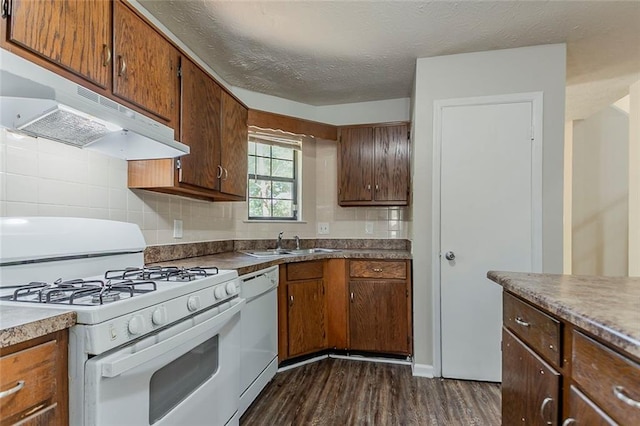 kitchen featuring white appliances, under cabinet range hood, a sink, dark wood finished floors, and decorative backsplash