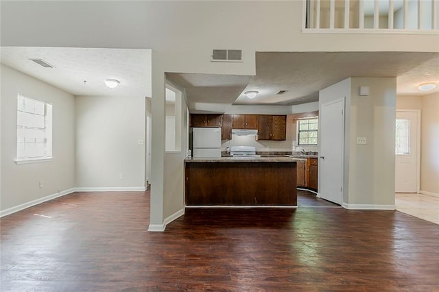 kitchen featuring freestanding refrigerator, under cabinet range hood, a peninsula, dark wood-style floors, and open floor plan
