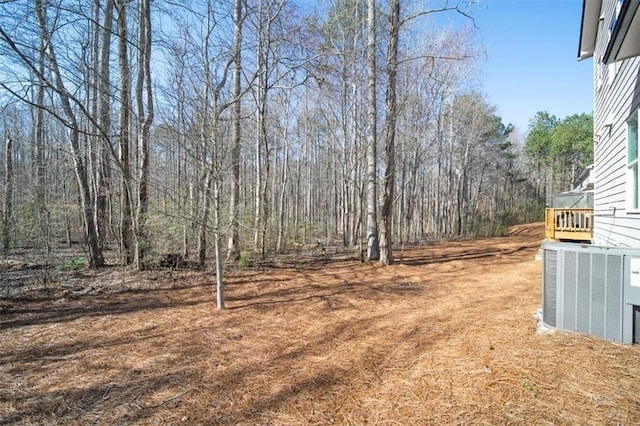 view of yard featuring central air condition unit and a wooded view