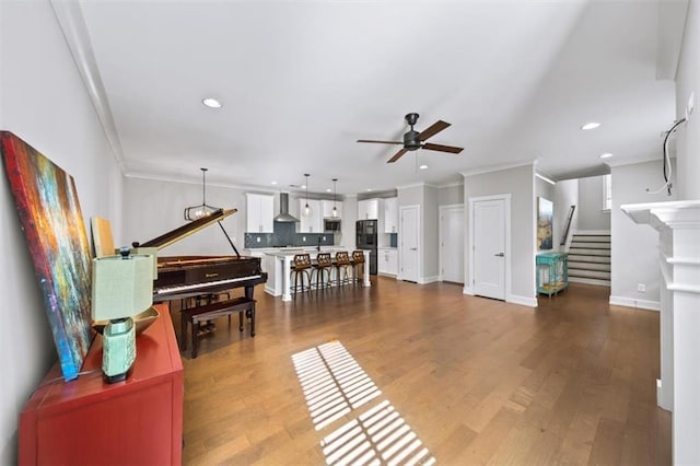 living area featuring stairway, ornamental molding, ceiling fan, and wood finished floors