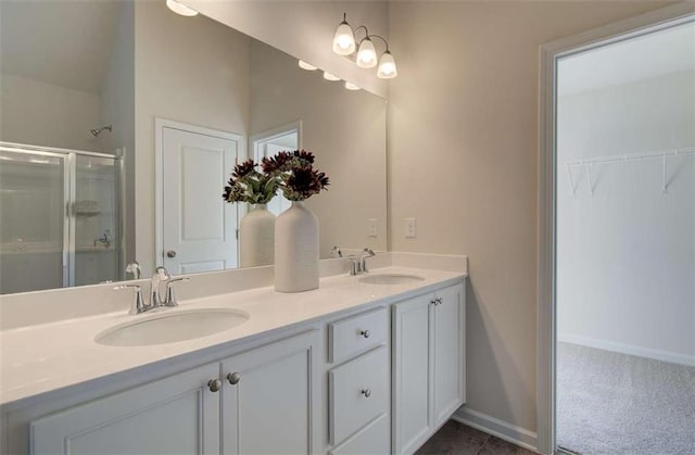 bathroom featuring a shower stall, double vanity, a sink, and baseboards