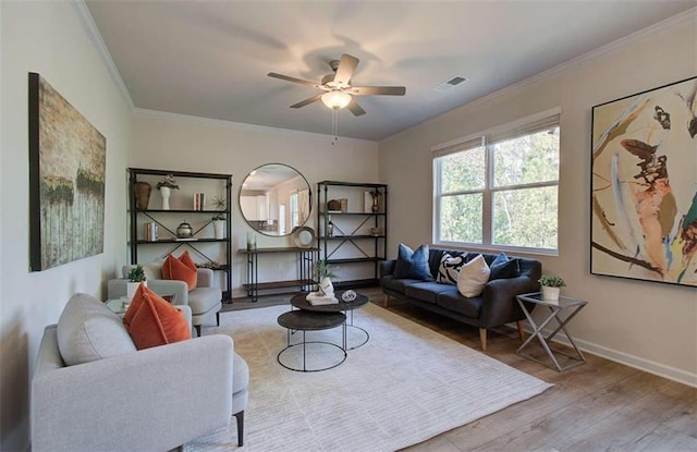 living room featuring ceiling fan, ornamental molding, visible vents, wood finished floors, and baseboards