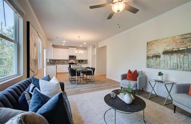 living area with baseboards, ornamental molding, recessed lighting, light wood-style floors, and ceiling fan with notable chandelier