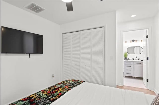 bedroom featuring ensuite bathroom, sink, light wood-type flooring, a closet, and ceiling fan