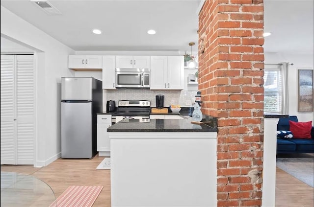 kitchen featuring white cabinets, backsplash, appliances with stainless steel finishes, dark stone counters, and light hardwood / wood-style flooring