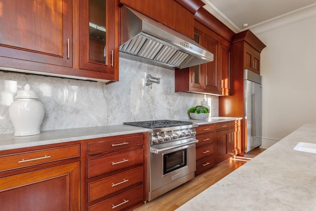 kitchen with wall chimney range hood, premium appliances, crown molding, decorative backsplash, and light wood-type flooring