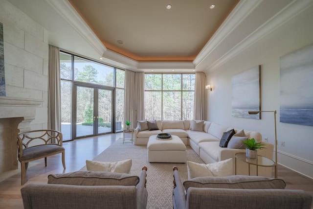 living room featuring french doors, a raised ceiling, light hardwood / wood-style flooring, ornamental molding, and a tiled fireplace